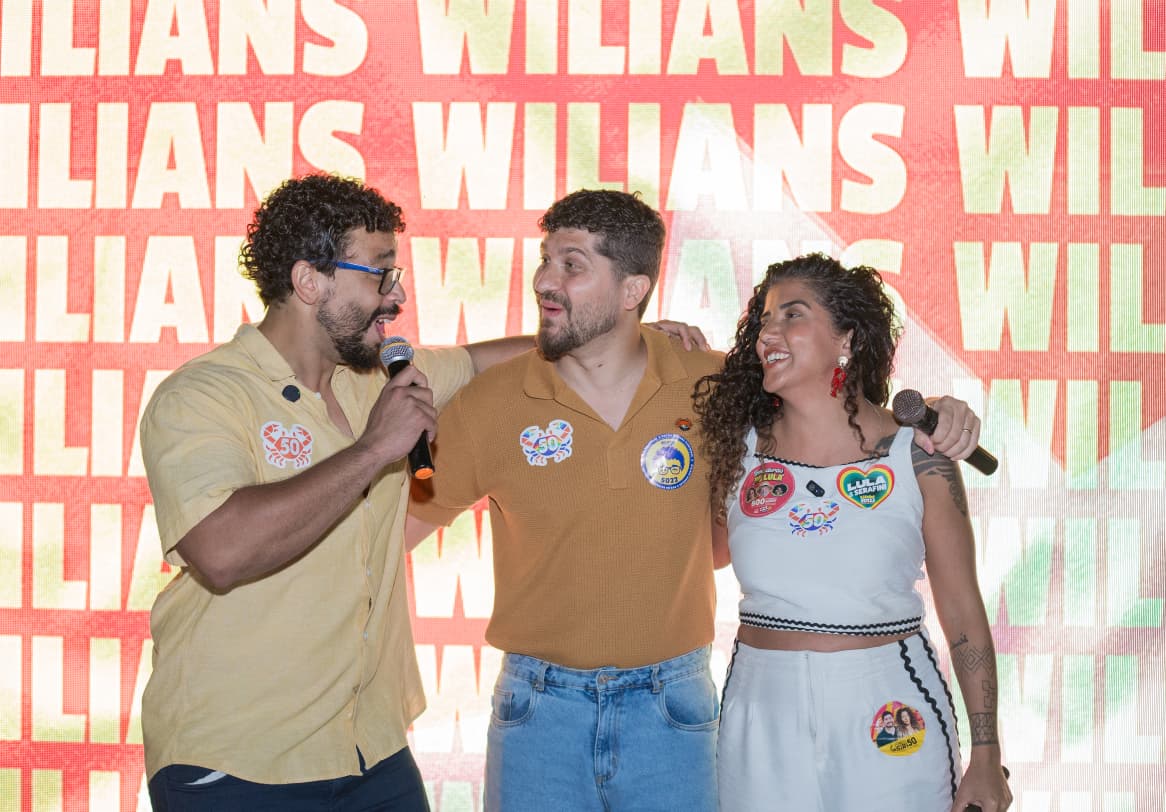 Wilians Douglas ao microfone no palco do lançamento, ao lado de William Siri e Juliana Carvalho